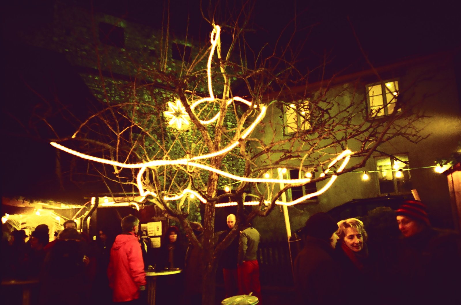 Innenhof am Abend mit Lichterketten und Menschen im Gespr&auml;ch (Lomo)